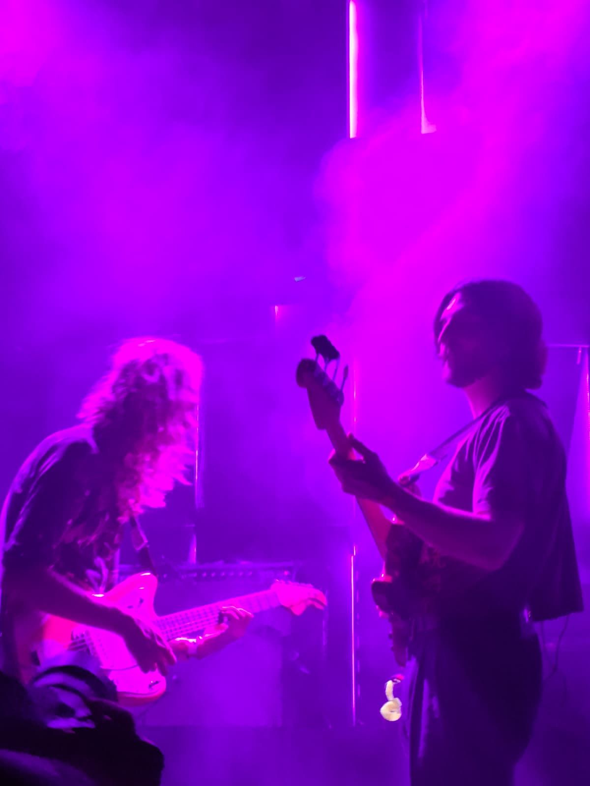 Mor ışık altında, sis dolu bir konserde karşılıklı durmuş gitar çalan YinYin grubunun iki üyesi